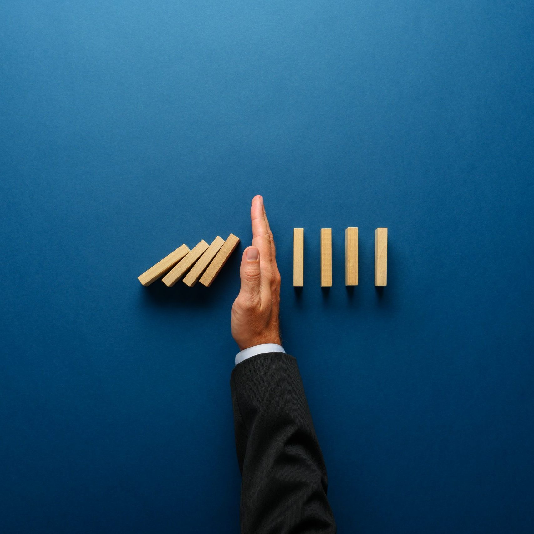 Top view  of businessman hand stopping falling dominos in a business crisis management conceptual image.