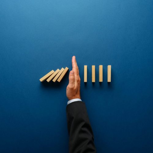 Top view  of businessman hand stopping falling dominos in a business crisis management conceptual image.